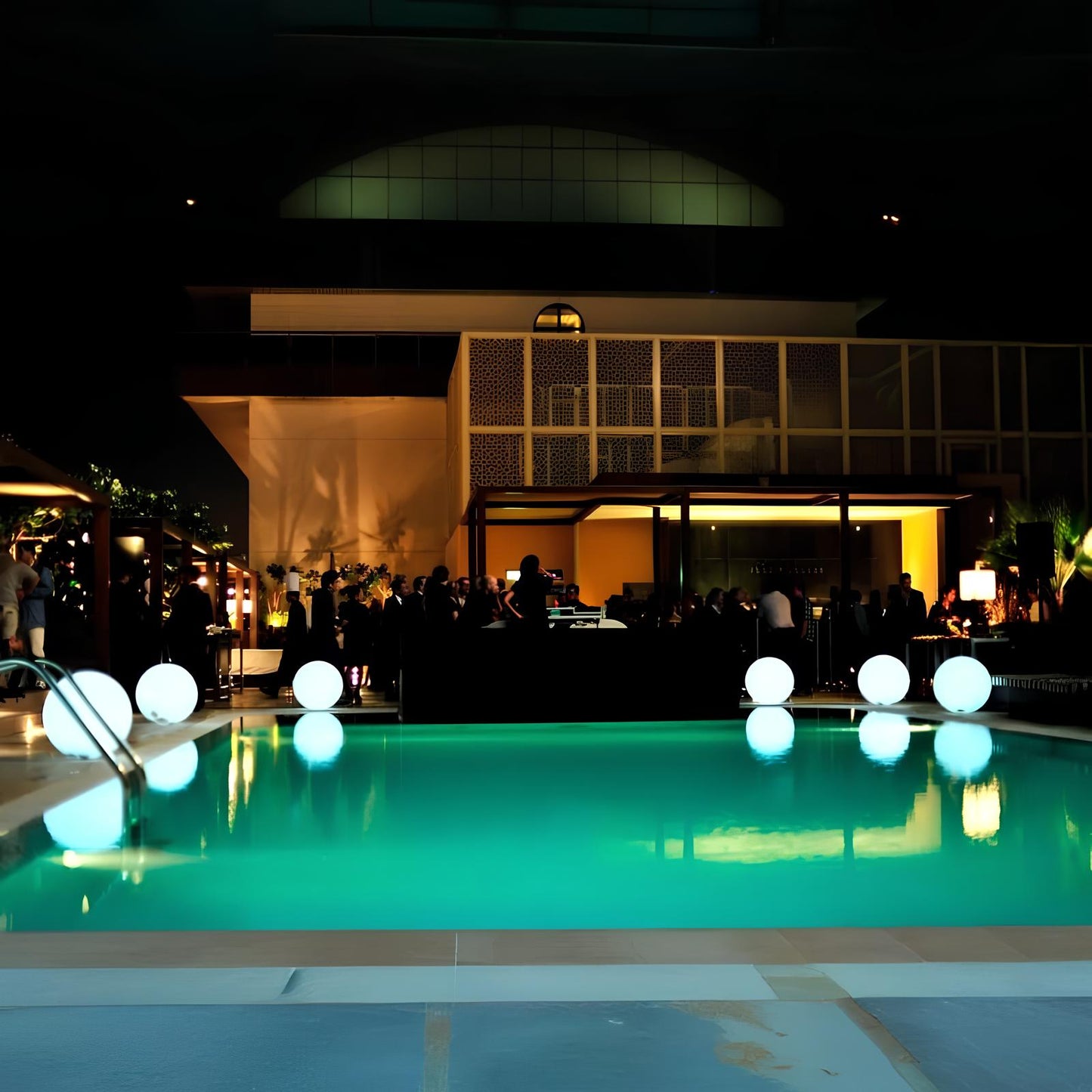 Beleuchteter Pool bei Nacht mit modernen Kugelleuchten und stilvoller Architektur im Hintergrund.