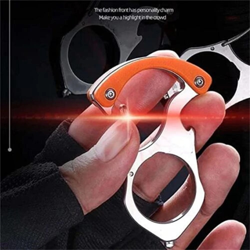 Hand håller en nyckelhållare i blank stål med orange grepp, med ytterligare hållare suddigt i bakgrunden mot mörk bakgrund. 1