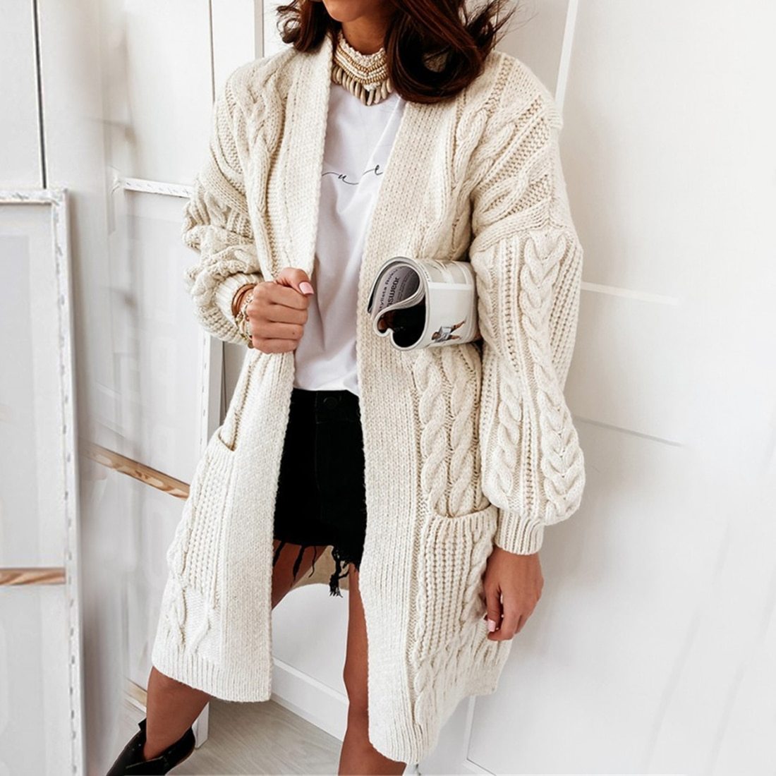 Frau trägt cremefarbenen Strickcardigan, Zopfmuster, lässig, modisch, Herbstmode, Damenbekleidung.