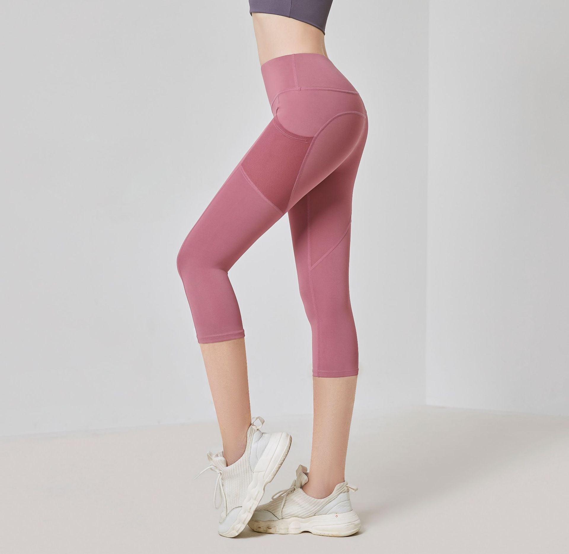 Frau in rosa Sportleggings und weißen Turnschuhen, seitlich stehend, vor neutralem Hintergrund.