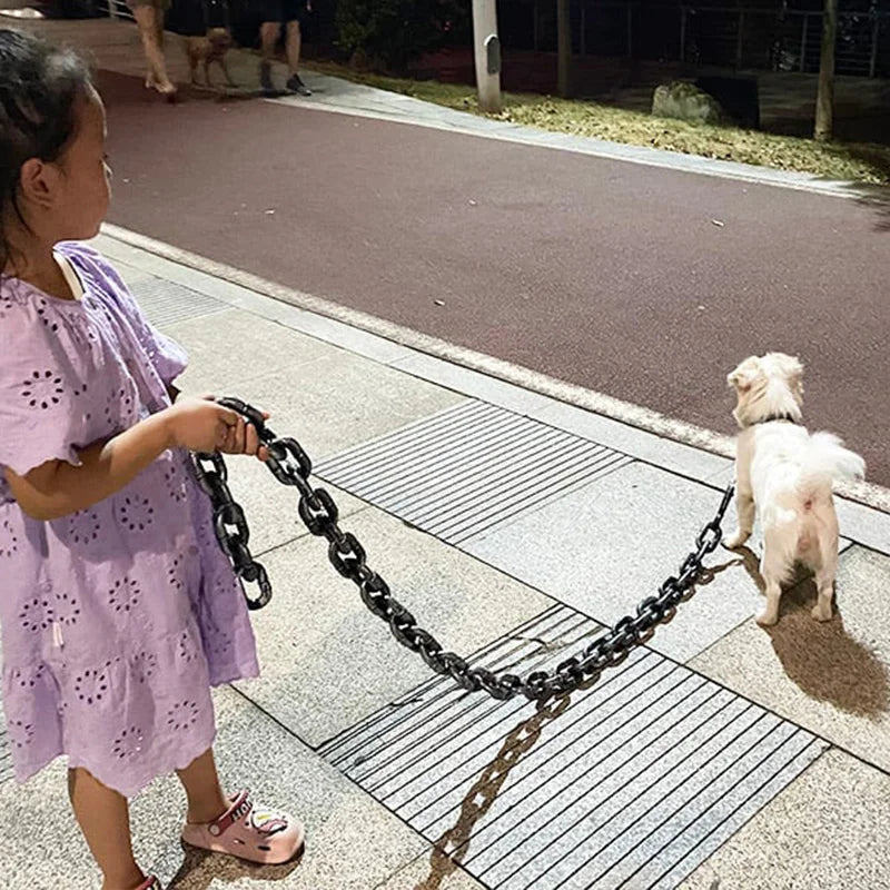 Mädchen in lila Kleid führt kleinen weißen Hund an großer Kette auf Gehweg spazieren.