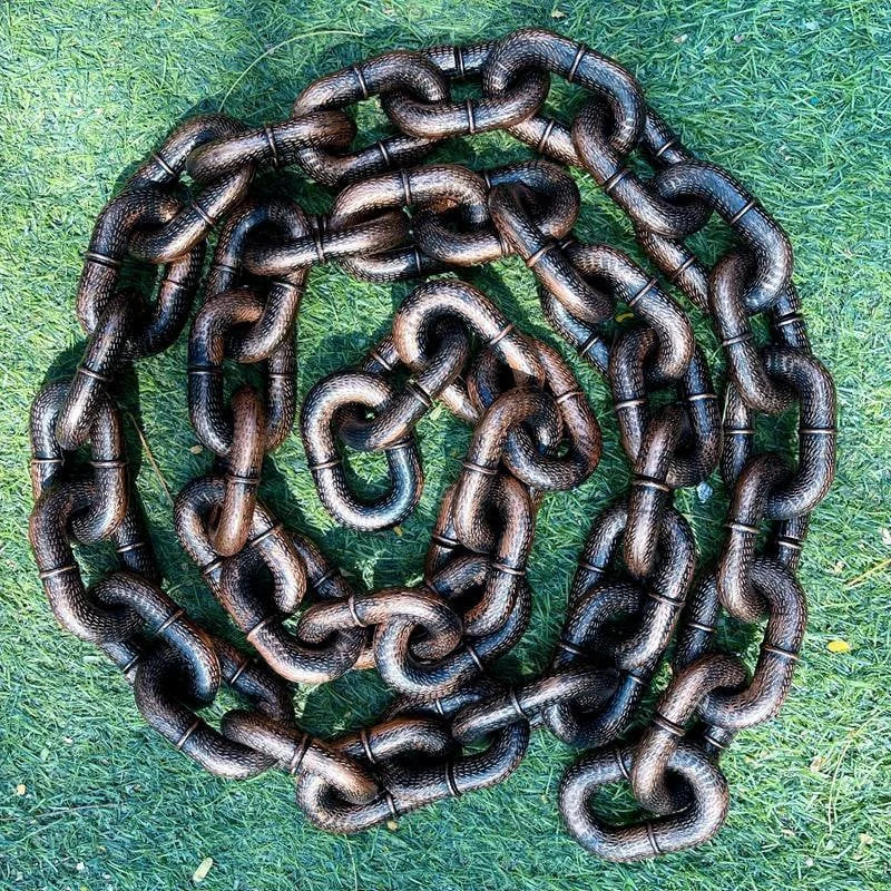 Schwarze Metallkette auf grünem Gras, schwere Glieder, robust, langlebig, Outdoor-Einsatz.