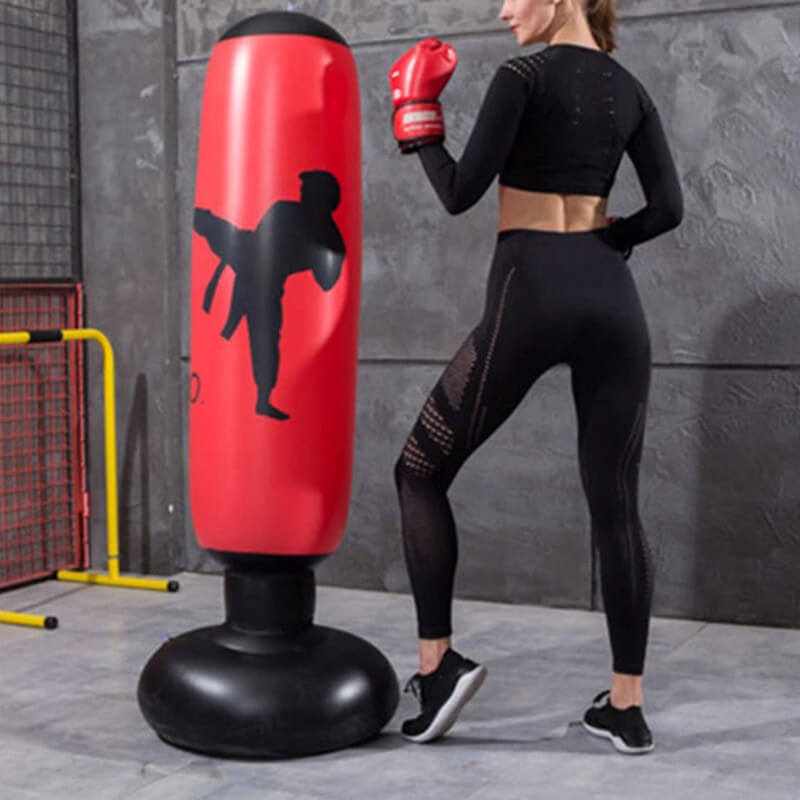 Frau trainiert mit rotem Boxsack, Fitnessstudio, Sportbekleidung, Indoor-Training, Selbstverteidigung.
