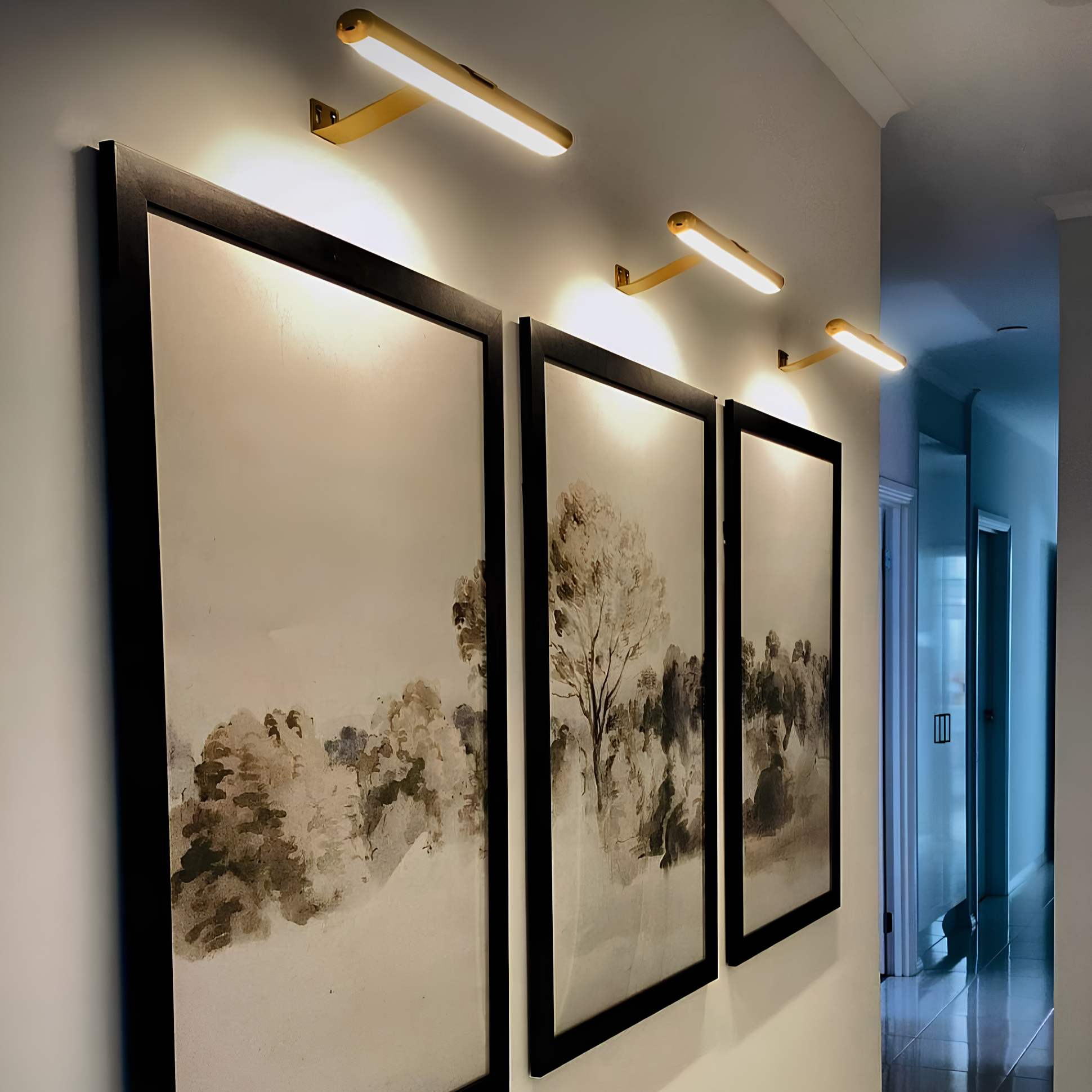 Moderne LED-Bilderleuchten in Gold über gerahmten Landschaftsgemälden im Flur.