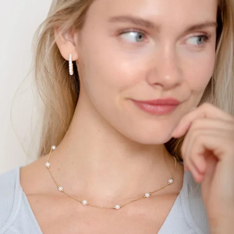 Frau mit goldener Halskette und Perlenohrring, eleganter Schmuck, Modeaccessoire.