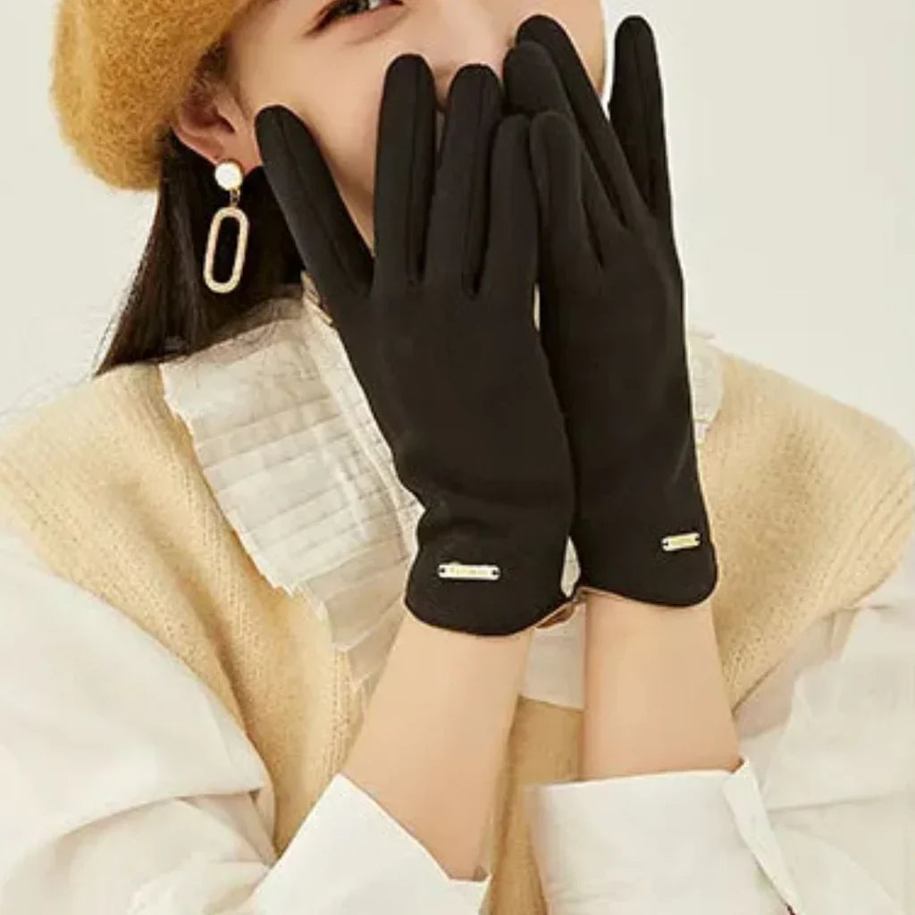 Frau mit schwarzen Handschuhen, beige Mütze, weißer Bluse und Ohrringen, stilvolle Wintermode.