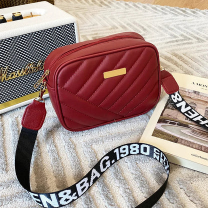 Rote Umhängetasche aus Leder mit gestepptem Design und verstellbarem Schultergurt.