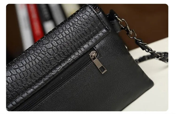 Schwarze Lederhandtasche mit Krokodilprägung, Reißverschluss und Kettengurt.