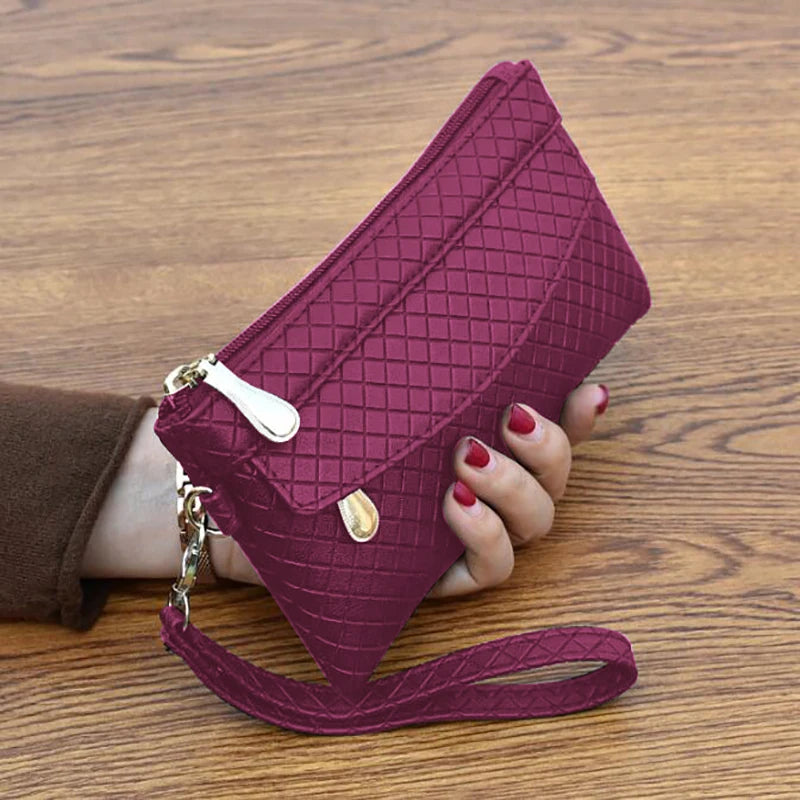 Damenhandtasche aus rotem Leder mit Rautenmuster, Reißverschluss und Trageriemen auf Holztisch.