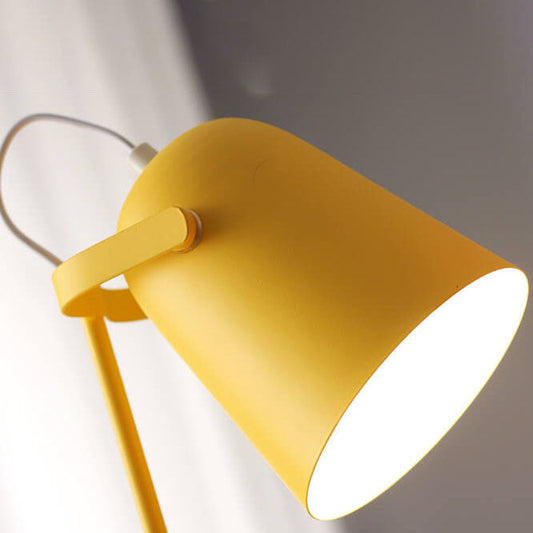 Närbild underifrån på den gula lampskärmen med mattlackerad yta, hållarmen och den vita sladden, med varmt ljus inuti skärmen. 2