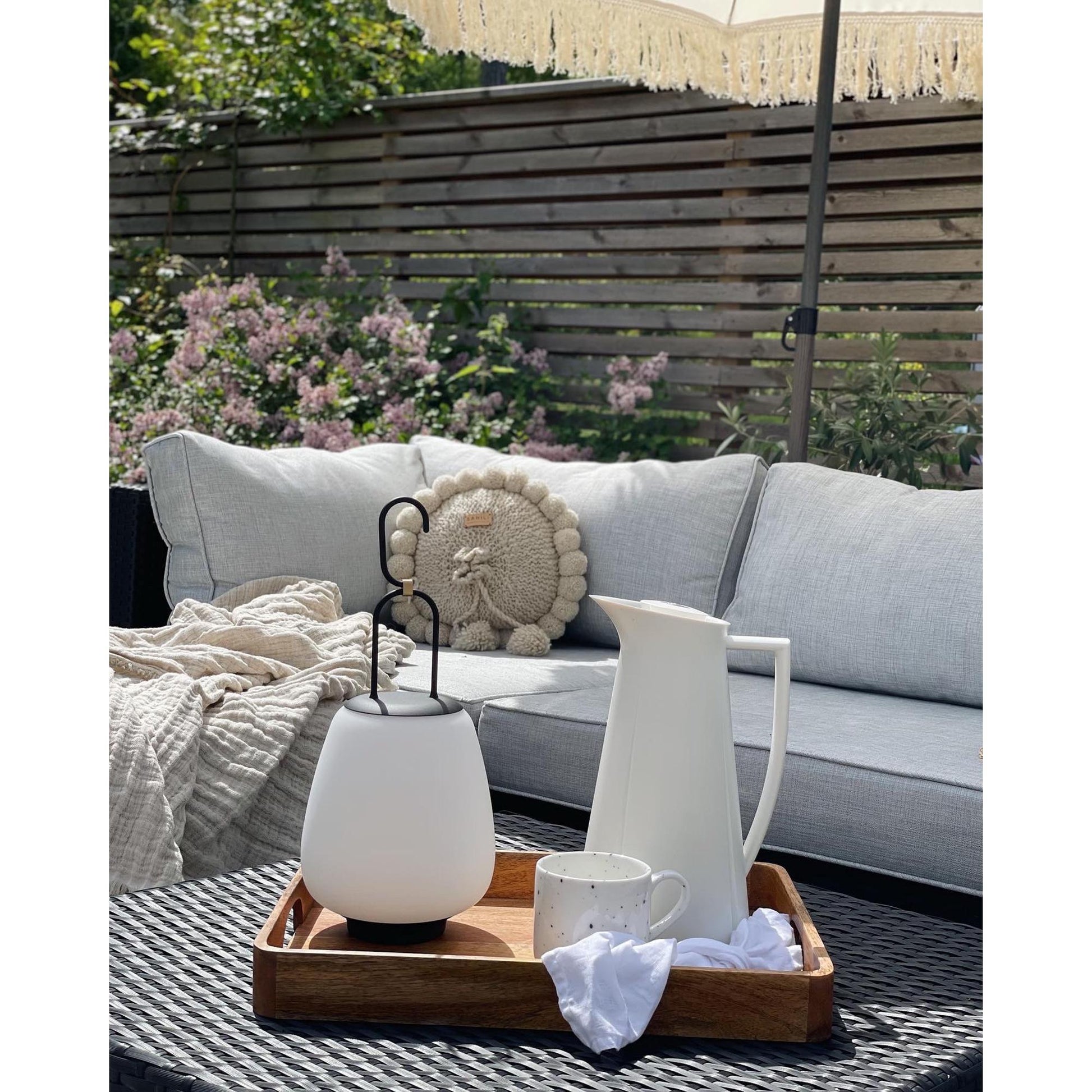 Weiße LED-Laterne und Kanne auf Holztablett, Gartenmöbel, Outdoor-Dekoration, Sommer.