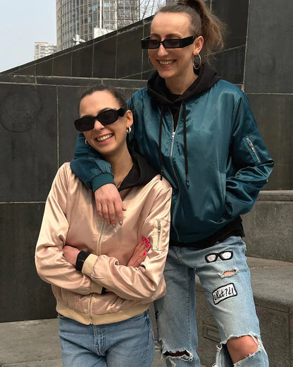 Zwei Frauen in modischen Bomberjacken, Sonnenbrillen, lässige Jeans, urbaner Hintergrund.