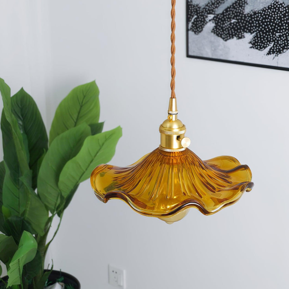 Gelbe Glas-Pendelleuchte mit Messingfassung, Vintage-Design, hängend, vor grüner Pflanze.