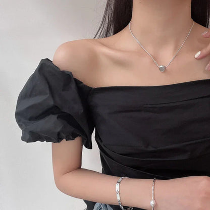 Frau trägt schwarzes Off-Shoulder-Kleid mit Puffärmeln und silberner Halskette.