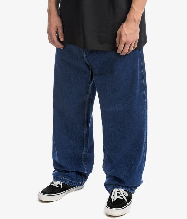 Mann trägt blaue Carhartt WIP Jeans, weites Bein, Baumwolle, lässiger Stil, schwarze Sneaker.