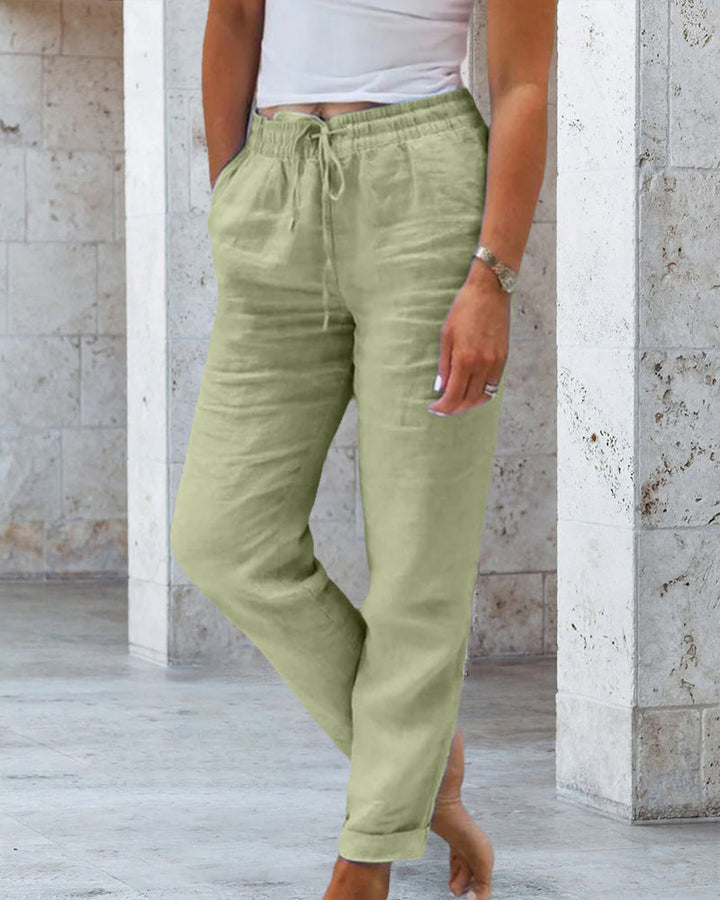 Frau in grüner Leinenhose, weißem Top, lässiger Look, Sommermode, beiger Hintergrund.