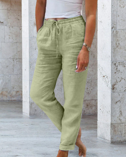 Frau in grüner Leinenhose, weißem Top, lässiger Look, Sommermode, beiger Hintergrund.