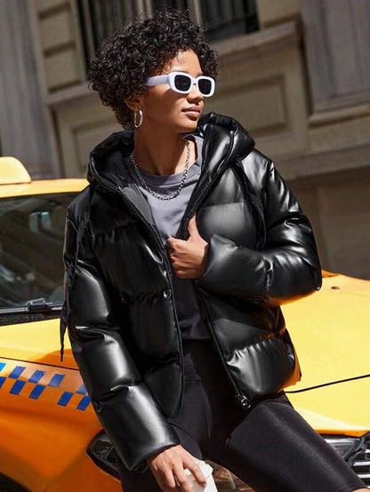Frau in schwarzer Daunenjacke vor gelbem Taxi, trägt weiße Sonnenbrille, modisch, urban.