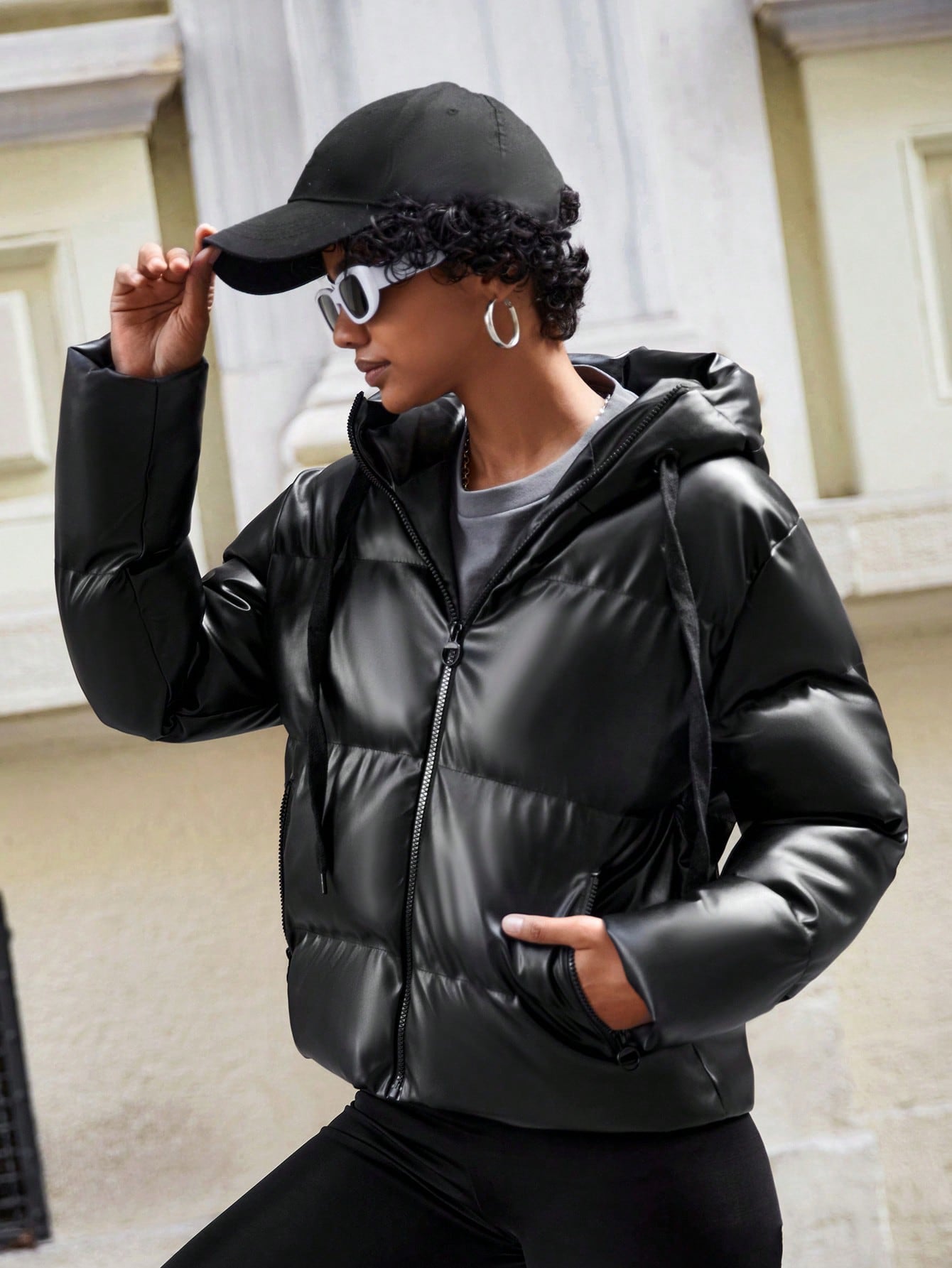 Frau in schwarzer Daunenjacke, Sonnenbrille und Mütze, modisch, urbaner Stil.
