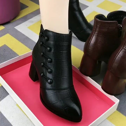 Schwarze Damenstiefeletten mit Absatz, Knopfdetails, Lederoptik, auf rosa Tablett.