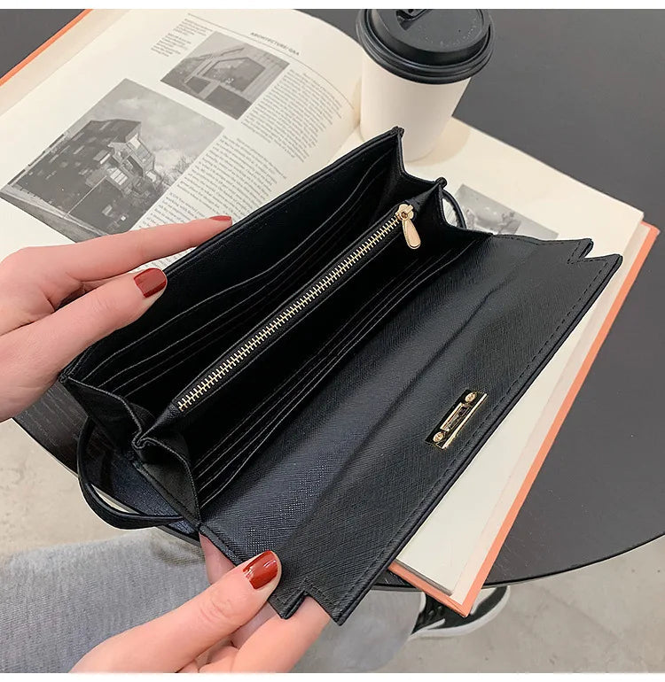 Schwarze Damen-Geldbörse aus Leder mit Reißverschluss, geöffnet auf Tisch mit Buch und Kaffeebecher.