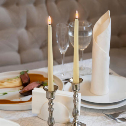 Zwei brennende weiße Kerzen in silbernen Kerzenhaltern auf elegant gedecktem Esstisch.