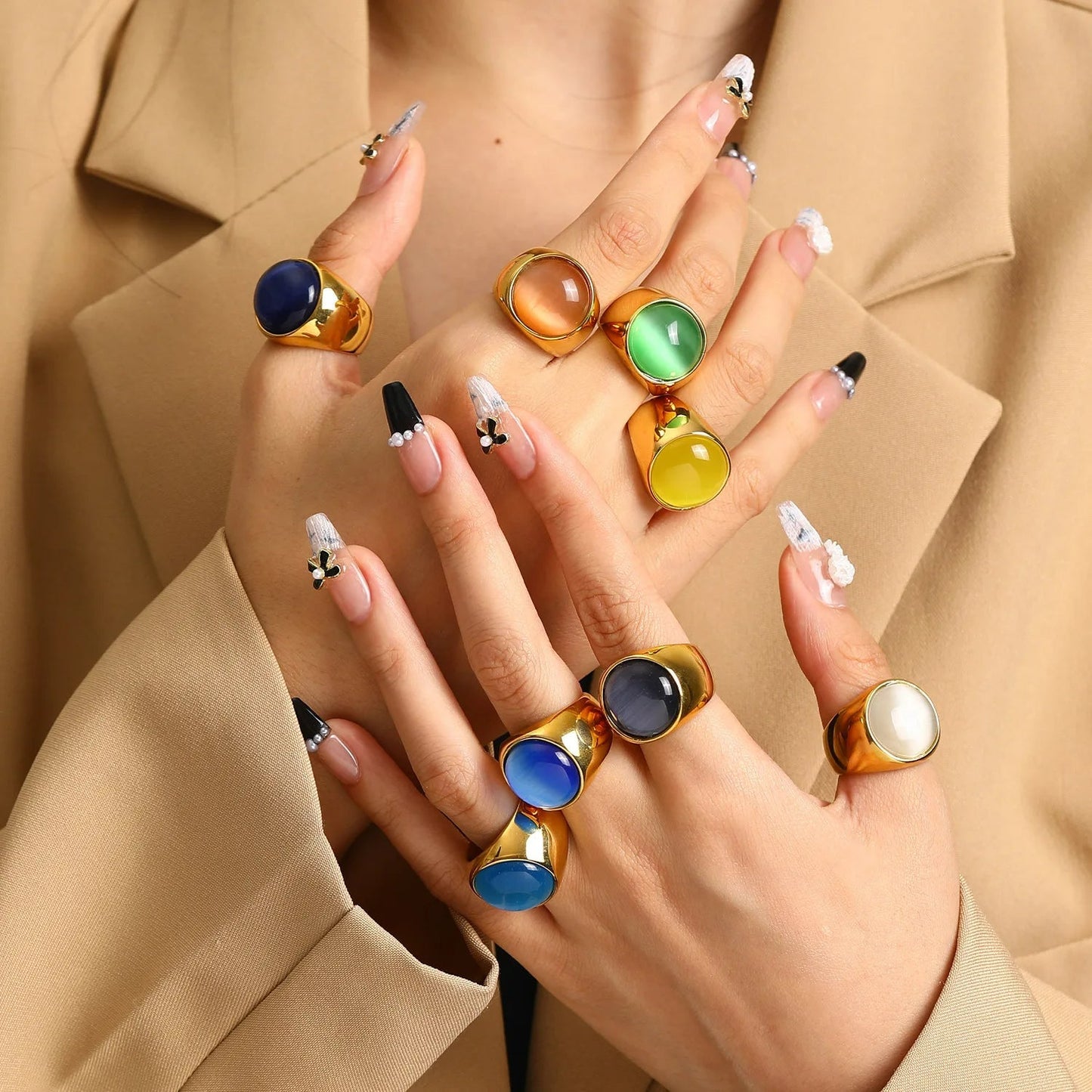 Frau mit goldenen Ringen, bunte Edelsteine, modische Nageldesigns, beige Blazer.