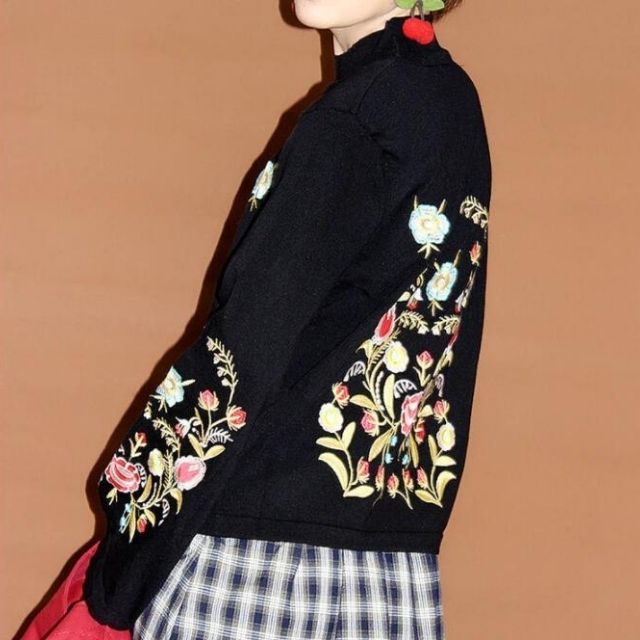 Frau in schwarzer Jacke mit bunter Blumenstickerei, kariertem Rock, modisch, elegant.