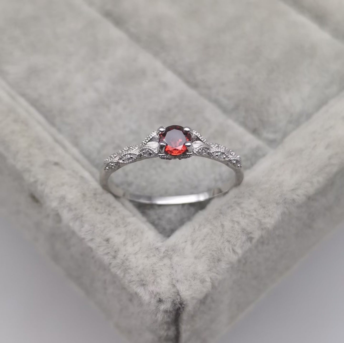 Silberring mit rotem Edelstein und Diamanten auf grauem Samtkissen.