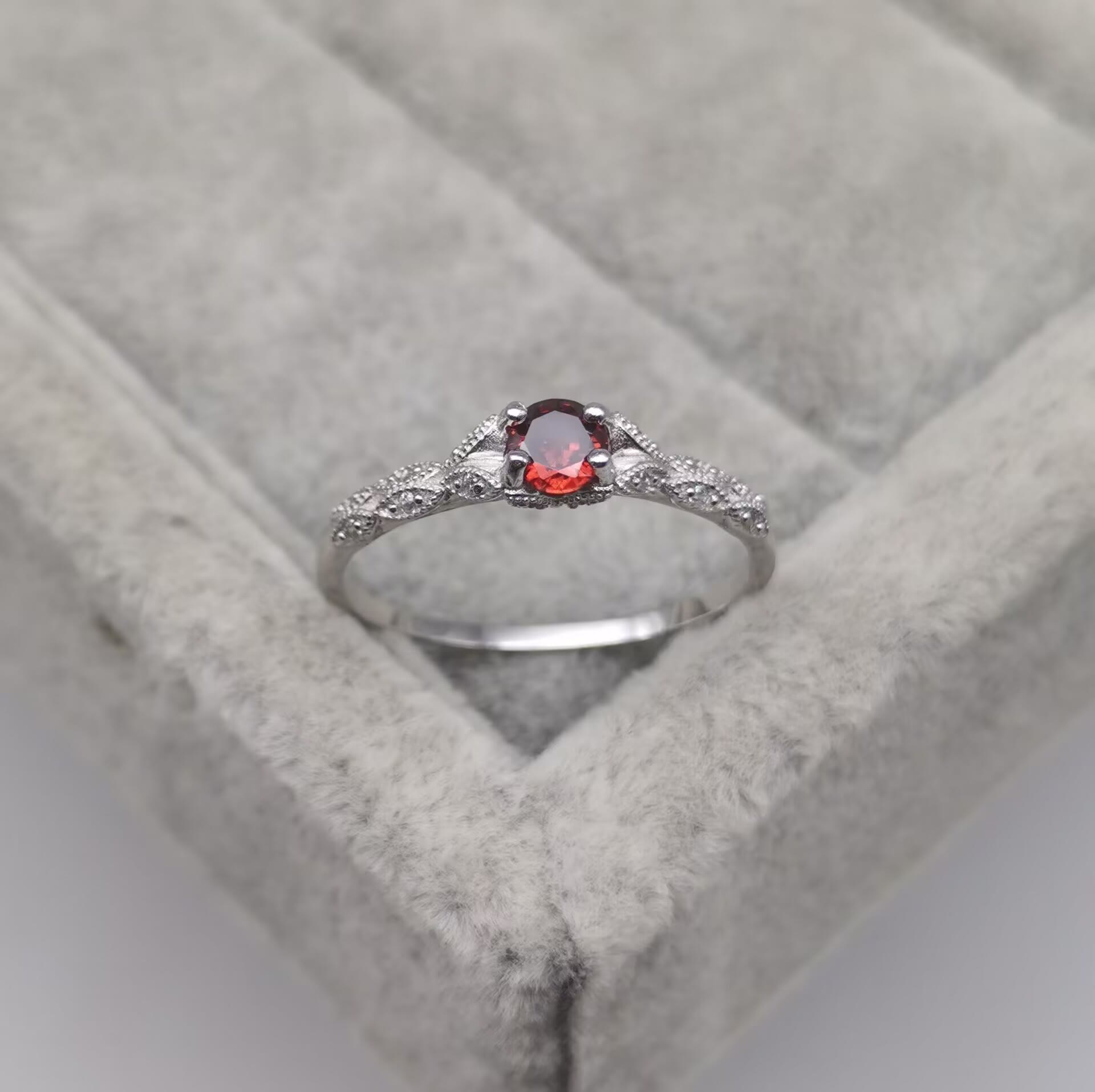 Silberring mit rotem Edelstein und Diamanten auf grauem Samtkissen.