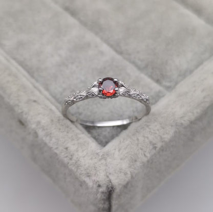 Silberring mit rotem Edelstein und Diamanten auf grauem Samtkissen.
