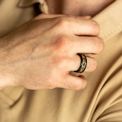 Männerhand mit schwarzem Edelstahlring, goldene Verzierung, elegantes Schmuckdesign.