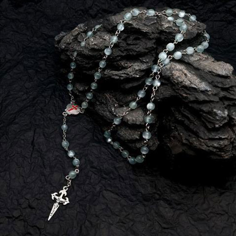 Silberne Rosenkranzkette mit grünen Perlen und Kreuzanhänger auf schwarzem Hintergrund.