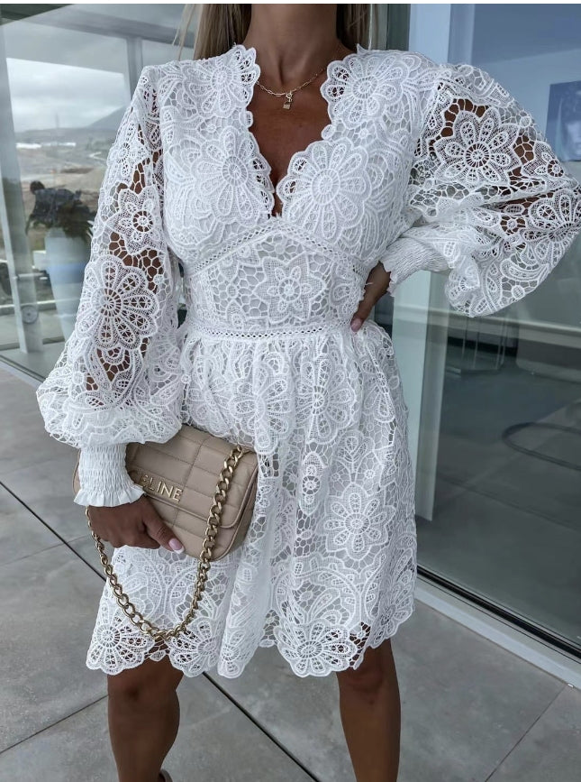 Frau in weißem Spitzenkleid mit langen Ärmeln, hält beige Handtasche mit Kettengurt.