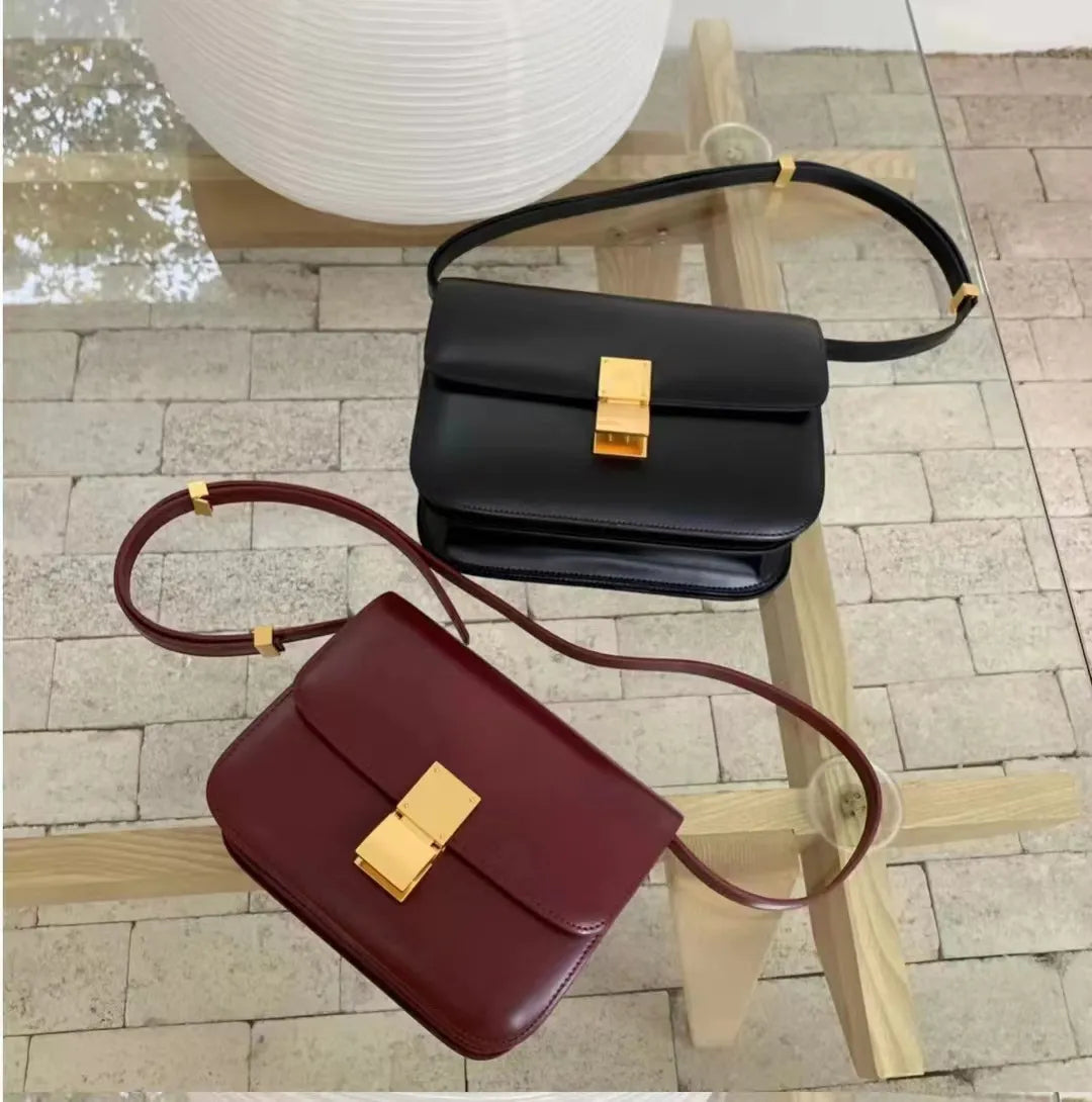 Zwei Designer-Ledertaschen, schwarz und rotbraun, mit goldenen Verschlüssen auf Holztisch.