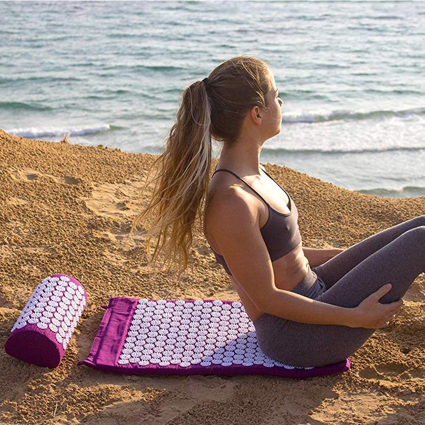 Frau auf lila Akupressurmatte am Strand, Entspannung, Yoga, Fitness, Selbstpflege, Meerblick.