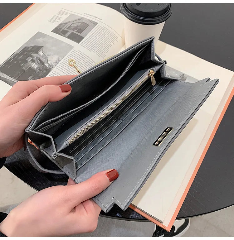 Graue Damen-Geldbörse aus Leder mit Reißverschluss, geöffnet auf Tisch mit Buch und Kaffeetasse.