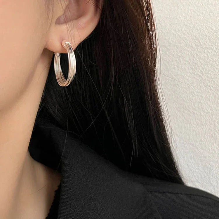 Silberne Creolen-Ohrringe an Frauenohr, eleganter Schmuck, modisches Accessoire.
