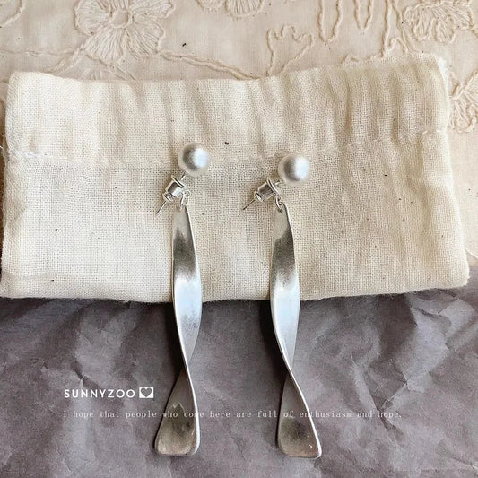 Silberne Ohrringe mit Perlen, modernes Design, auf beigem Stoff, Schmuckaccessoire.