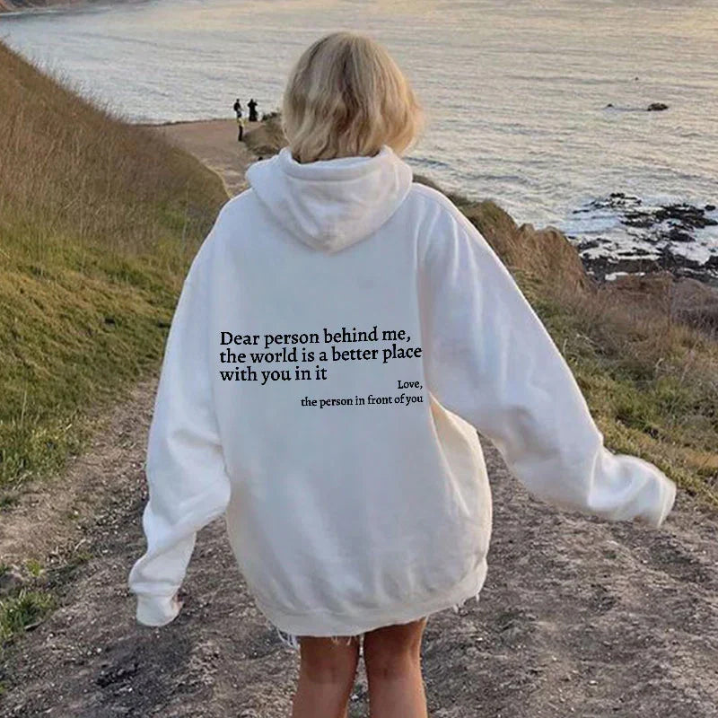 Weiße Oversize-Hoodie mit Rückenaufdruck, Frau am Küstenweg, lässige Mode.