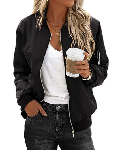 Frau in schwarzer Bomberjacke, weißem T-Shirt, hält Kaffeebecher, lässiger Streetstyle-Look.
