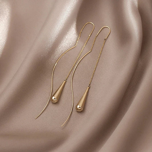 Goldene Ohrringe auf beigem Seidenstoff, minimalistisches Design, eleganter Schmuck.