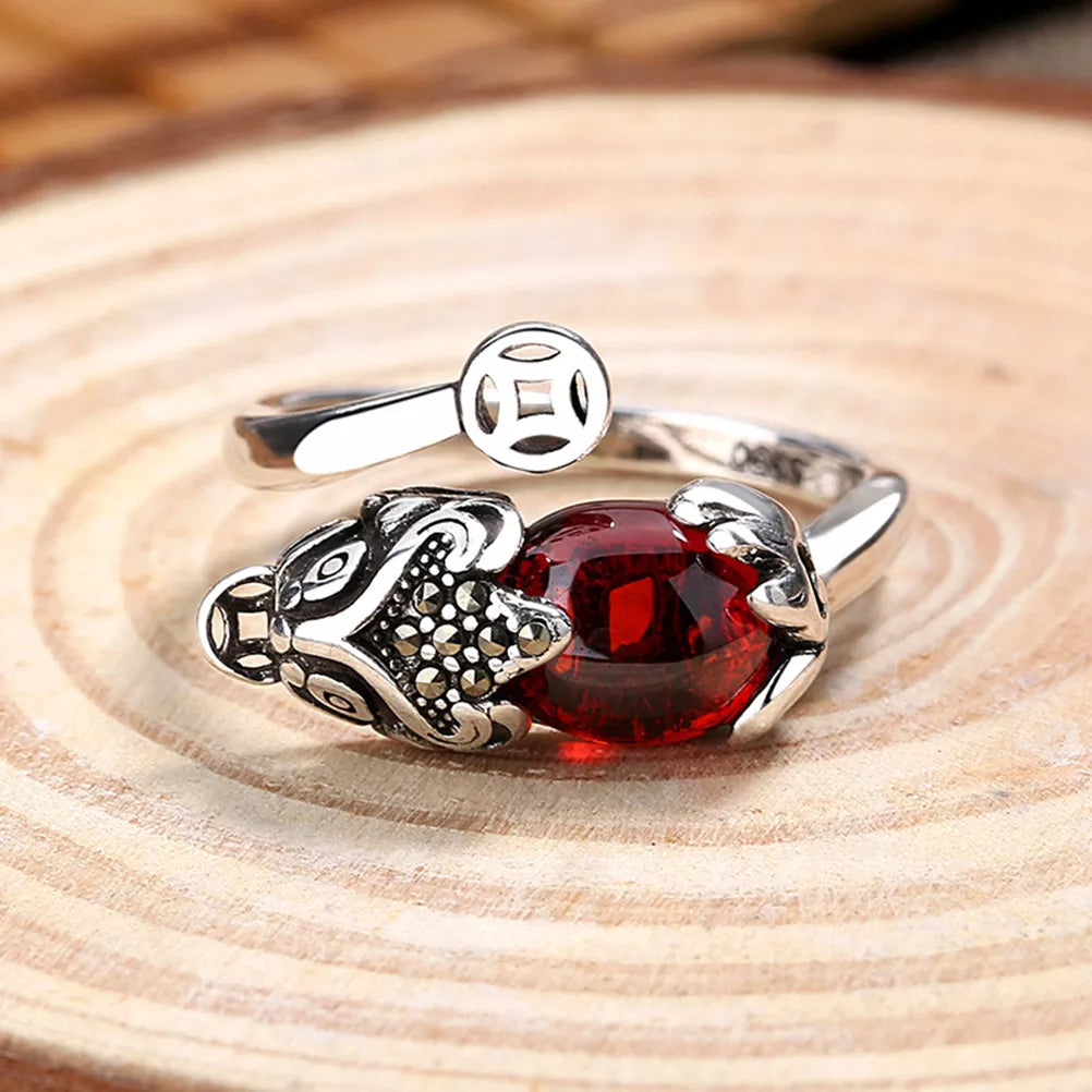 Silberring mit rotem Edelstein und Löwenkopf-Design auf Holzuntergrund.
