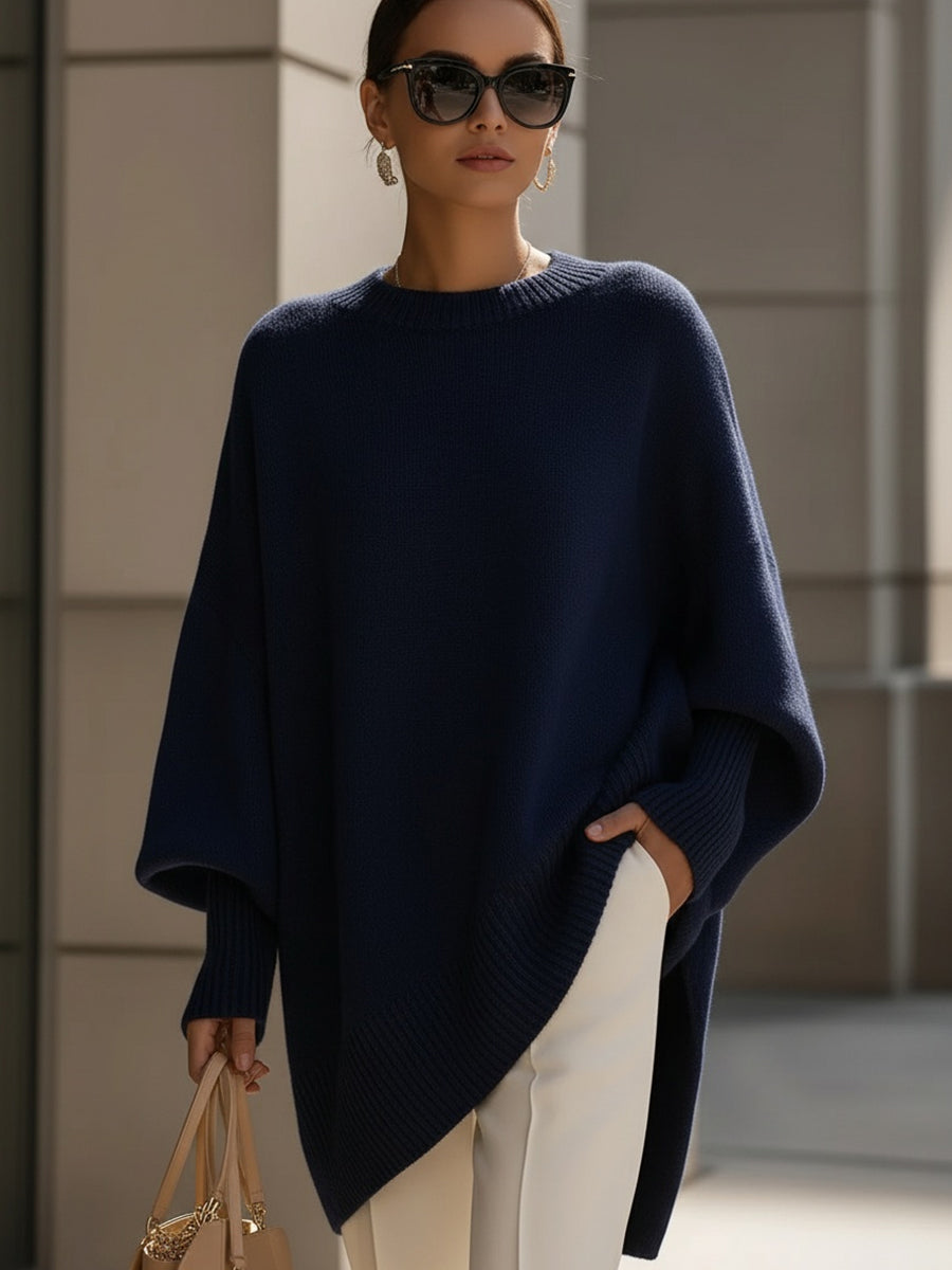 Modell i marinblå stickad poncho med solglasögon, vita byxor och beige handväska 9