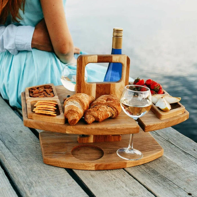 Picknicktisch aus Holz mit Weinhalter, Croissants, Erdbeeren, Käse, Nüssen und Crackern am See.
