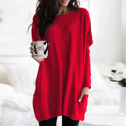 Frau in rotem Oversize-Pullover hält Tasse, gemütliche Wintermode, Wohnzimmer-Hintergrund.