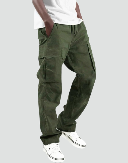 Man bär olivgröna cargobyxor med stora sidfickor och dragsko i midjan, vit t-shirt och vita sneakers, snett framifrån. 1