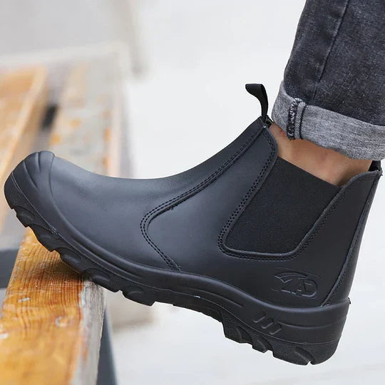 Svart känga i läder med resårinsats, buren av en person med uppvikta jeans på en trätrappa 1