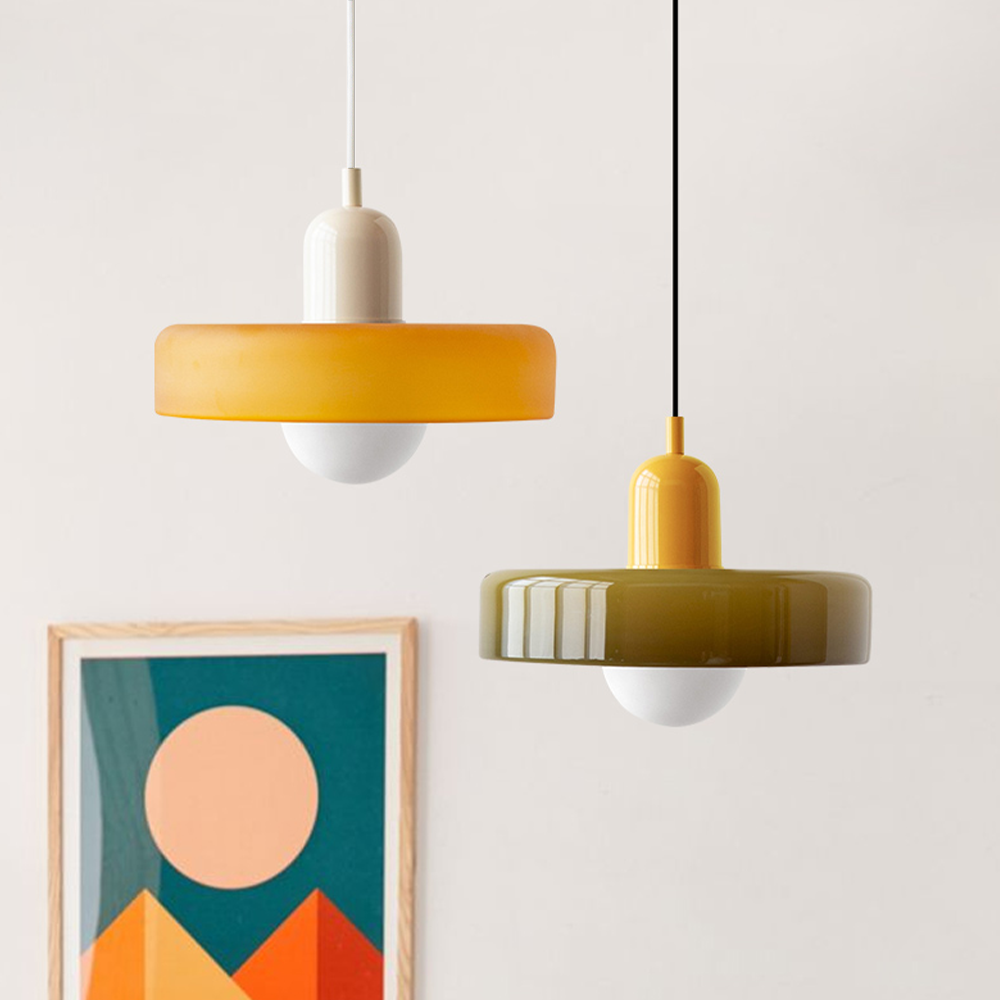 Zwei moderne Pendelleuchten, gelb und olivgrün, aus Glas, vor minimalistischem Hintergrund.