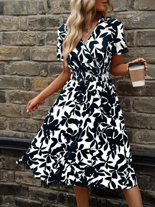 Frau im schwarz-weiß geblümten Sommerkleid mit Kaffeebecher vor Ziegelwand.